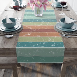 May include: A teal, green, orange, and brown striped table runner with a distressed, vintage look. The runner is on a wooden table with two place settings.