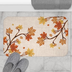 May include: A beige bath mat with a pattern of brown branches and orange, yellow, and brown maple leaves.