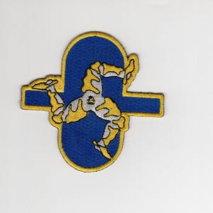 May include: Embroidered patch featuring the Triskelion of the Isle of Man. The design includes three armored legs in yellow, set against a blue background with a yellow border. The patch is likely for clothing or accessories.