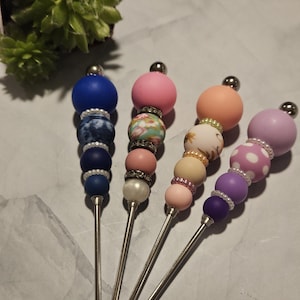 Puede incluir: Cuatro palitos de agitación con cuentas de colores y mangos de metal plateado. Las cuentas son de silicona y presentan diferentes patrones, incluyendo lunares, flores y diseños abstractos. Los palitos son perfectos para mezclar bebidas o café.