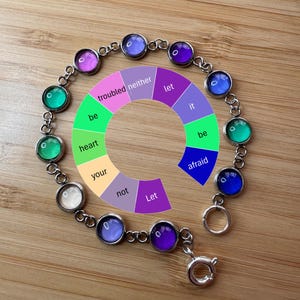 May include: A silver chain bracelet with colorful glass beads. Each bead has a word printed on it, including "let", "be", "afraid", "heart", "your", "not", "troubled", "neither", "it".