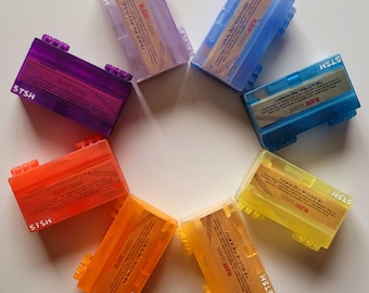 May include: Seven colorful plastic containers with the text "RAW CLASSIC" and "STSH" printed on them. The containers are arranged in a circle on a white surface.