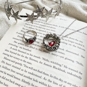 An open book with a ring, necklace, and crown of stars on it. The book is Kingdom of Ash from the Throne of Glass series and the items represent Manon Blackbeak and Dorian Havilliard, hence Hello Princeling