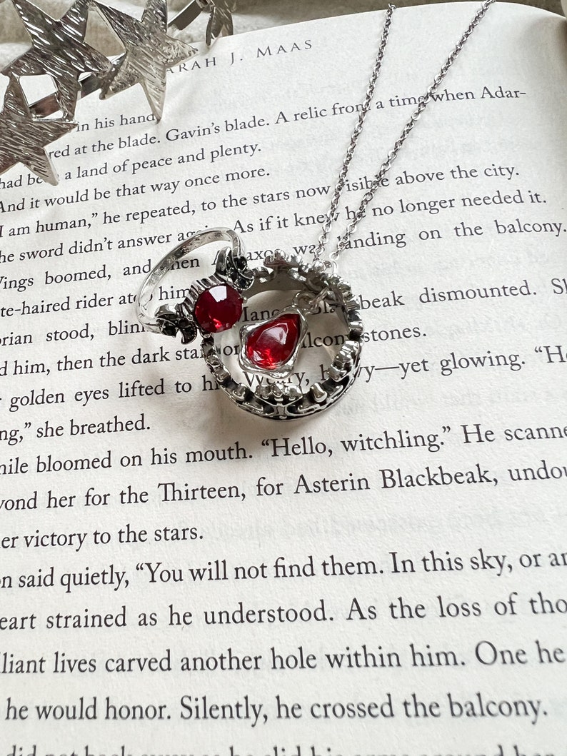 An open book with a ring, necklace, and crown of stars on it. The book is Kingdom of Ash from the Throne of Glass series and the items represent Manon Blackbeak and Dorian Havilliard, hence Hello Princeling
