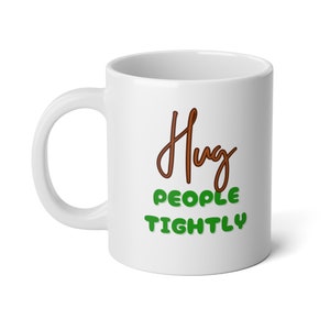 Peut inclure: Une tasse à café en céramique blanche avec le texte "Hug People Tightly" en lettres brunes et vertes.