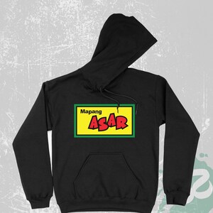 Pode incluir: Camisola de capuz preta com um gráfico retangular amarelo e verde que diz "Mapang Asar" em letras vermelhas.