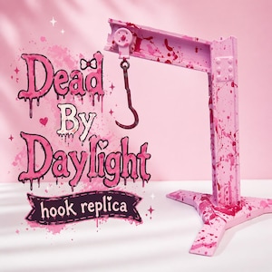 May include: A pink hook replica with blood splatter details, inspired by "Dead By Daylight." The replica features a metal hook hanging from a pink beam, mounted on a four-legged base. The text "Dead By Daylight" and "hook replica" are also visible.
