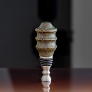 May include: A wooden bottle stopper with a green and brown wood grain pattern and a silver metal base.