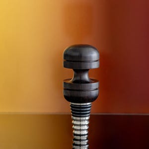 May include: A black wooden bottle stopper with a silver threaded base. The stopper has a rounded top and a grooved design.