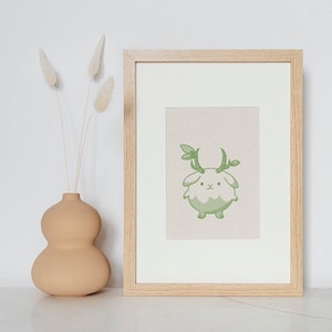 May include: A framed print of a green cartoon creature with antlers. The creature has a white body and a light green face. The print is on a light beige background and is framed in a light wood frame.