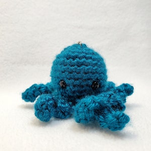 May include: A teal blue crocheted octopus with black eyes. The octopus is a small plush toy.