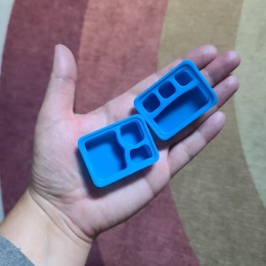 May include: A blue plastic container with multiple compartments, open to reveal the inside. The container is designed for portioning food.