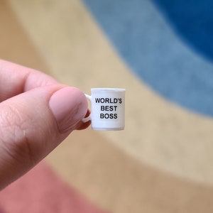 May include: A small white ceramic mug with a black handle and the text "WORLD'S BEST BOSS" printed on the front.