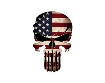 May include: A skull graphic featuring the American flag design. The skull has a distressed, vintage style with a black outline and white teeth. The flag is red, white, and blue with a faded, worn look.
