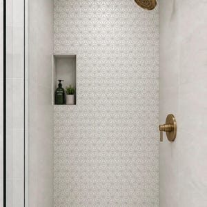 May include: A shower stall featuring white geometric star-patterned wall tiles, a recessed niche containing a dark green bottle and a small potted plant, and brushed brass shower fixtures including a round showerhead and a single-handle valve.