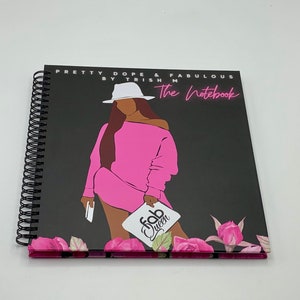 Peut inclure: Un carnet &agrave; spirales noir avec une illustration rose et noire d'une femme portant un chapeau blanc et une robe rose. Le carnet porte le texte "Pretty Dope & Fabulous by Trish M The Notebook" et "Fab Queen" sur la couverture.