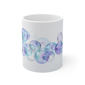 May include: White ceramic mug featuring a cluster of iridescent bubbles in shades of blue, purple, and green. The bubbles appear to float around the mug, creating a whimsical and artistic design. The mug has a simple, clean design.