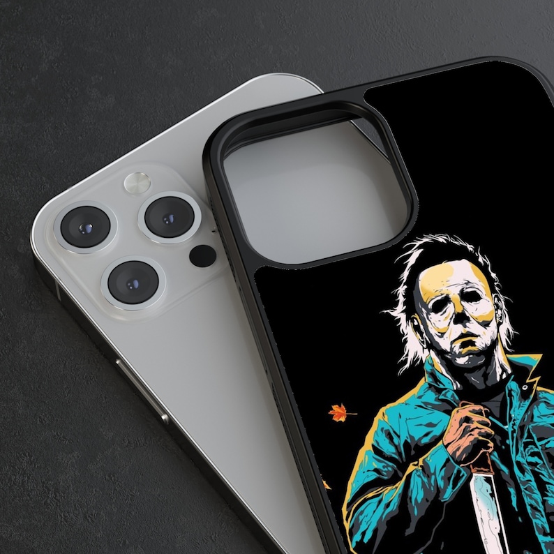 May include: Black phone case with a graphic of Michael Myers from the Halloween franchise. The case has a black background with a white outline of Michael Myers holding a knife. The case is designed for an iPhone.