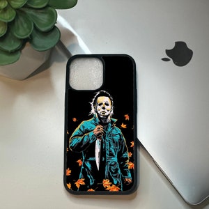 May include: Black phone case with a graphic of Michael Myers from the Halloween movies holding a knife. The background is black with orange and yellow leaves.