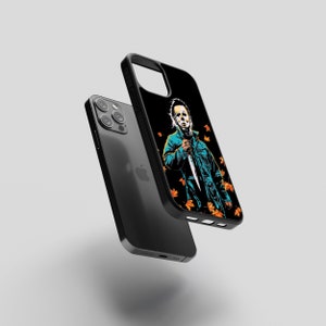 May include: Black iPhone case with a graphic of a masked figure holding a knife, surrounded by orange and yellow leaves. The figure is wearing a blue jumpsuit.