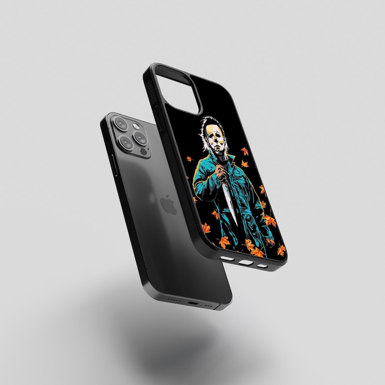 May include: Black iPhone case with a graphic of a masked figure holding a knife, surrounded by orange and yellow leaves. The figure is wearing a blue jumpsuit.