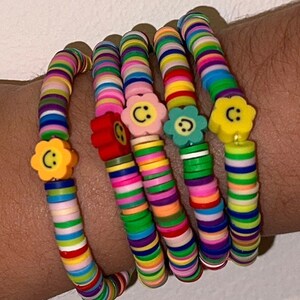 May include: Four colorful beaded bracelets with smiley face flower charms. Each bracelet is made of small, colorful beads stacked on top of each other.