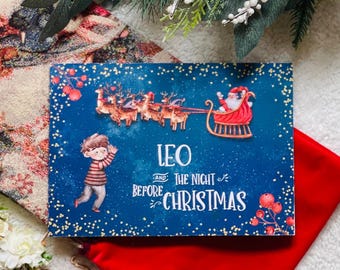May include: A Christmas-themed card with a blue background featuring Santa Claus in his sleigh, reindeer, and a child. The card reads "Leo and The Night Before Christmas." Decorative elements include berries and a festive arrangement.