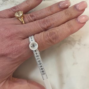 Op de afbeelding: Een witte plastic ringmaat met de nummers 6 tot en met 17 erop gedrukt. De ringmaat wordt gebruikt om een vinger te meten.