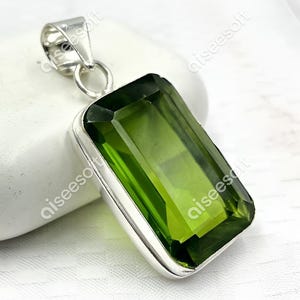 Könnte beinhalten: Ein silberner Anhänger mit einem großen, rechteckigen, grünen Edelstein. Der Edelstein ist in einer facettierten Form geschliffen.