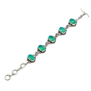 Könnte beinhalten: Silberarmband mit ovalen, hellgrünen Edelsteinen. Das Armband hat ein dekoratives Blumendesign zwischen jedem Stein und einen Knebelverschluss. Die Edelsteine sind in Silbermetall gefasst.