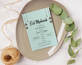 Puede incluir: Una tarjeta de invitación azul claro con el texto "Eid Mubarak" en una fuente decorativa. La tarjeta está decorada con lunas crecientes y linternas. El texto "You Are Invited To Eid Dinner Hosted By Javed & Nafisa" está impreso en la tarjeta. La fecha y la hora del evento se enumeran como "Wednesday, April 10th, 2024, 5:30 pm". La dirección y la información de RSVP también están incluidas.