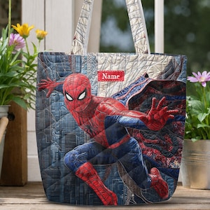May include: A quilted tote bag featuring a graphic of the character Spider-Man in a dynamic pose. The bag has a blue and red color scheme with a city skyline pattern and a rectangular red patch at the top center with the white text Name.