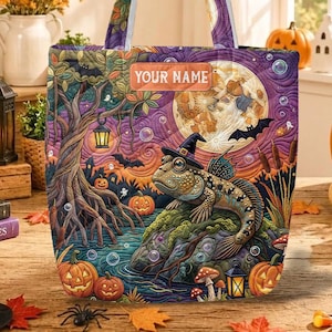 May include: A quilted tote bag featuring a colorful Halloween-themed illustration of a fish wearing a witch hat sitting on a rock, with a full moon, trees, and pumpkins in the background. The text "YOUR NAME" is printed on a rectangular label.