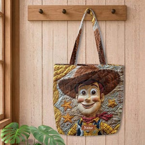 May include: A quilted tote bag featuring a graphic of a cowboy character wearing a brown hat and a yellow shirt with a red neckerchief. The background has a yellow star pattern and a brown rectangular patch with the text Name printed in white.