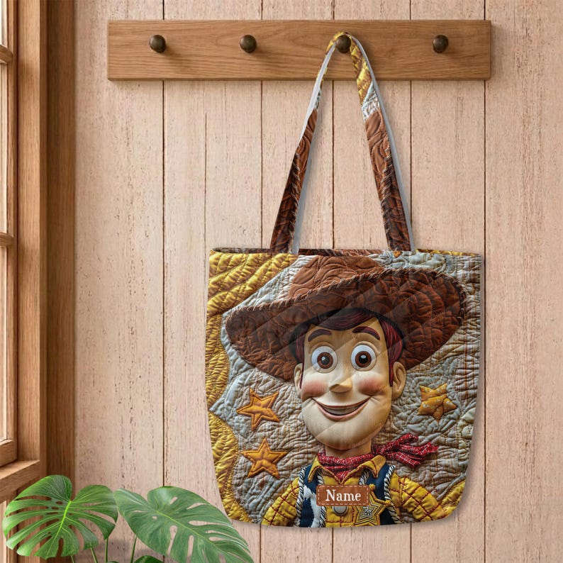 May include: A quilted tote bag featuring a graphic of a cowboy character wearing a brown hat and a yellow shirt with a red neckerchief. The background has a yellow star pattern and a brown rectangular patch with the text Name printed in white.