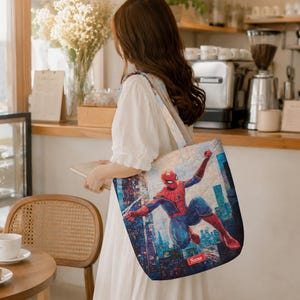 May include: A rectangular fabric tote bag featuring a vibrant, full-color graphic of the superhero Spider-Man in a dynamic leaping pose against a stylized city skyline. The design includes a small red rectangular label with the text Name.