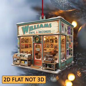 Op de afbeelding: Een plat, tweedimensionaal hangend ornament in de vorm van een platenwinkel. Het bord toont de tekst Williams Vinyl & Records. De buitenkant bevat posters, een rode deur met een open-bord en vinylplaten die in de winkel staan.