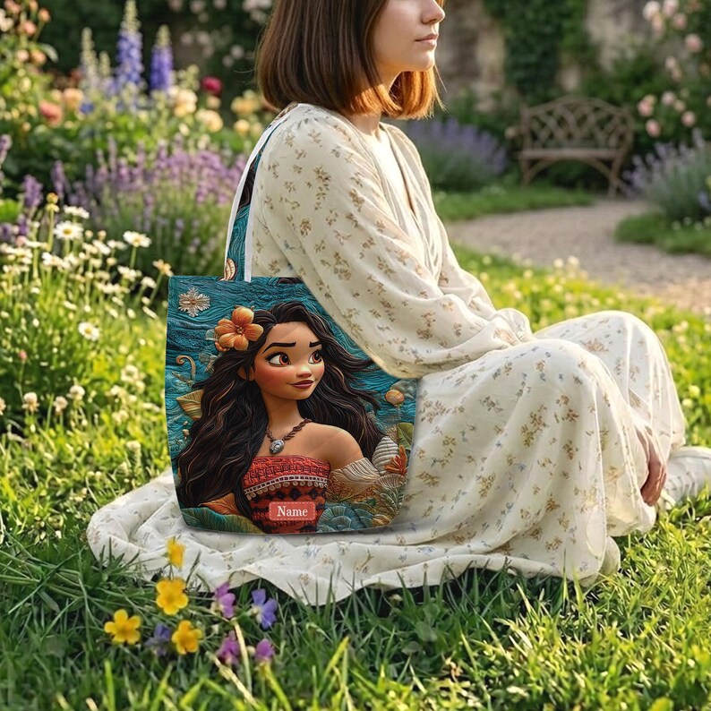 May include: A rectangular tote bag featuring a vibrant illustration of a long-haired character with a flower in their hair, wearing a patterned top and a necklace. The bag has a teal background with ocean-like textures and a red rectangular label with the text Name.