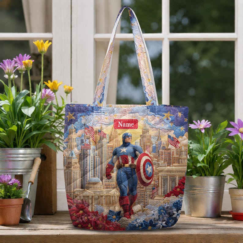 May include: A quilted tote bag featuring a graphic of Captain America standing in front of a city skyline with American flags. The bag has a rectangular red label with the text Name at the top center and two shoulder straps with a matching pattern.