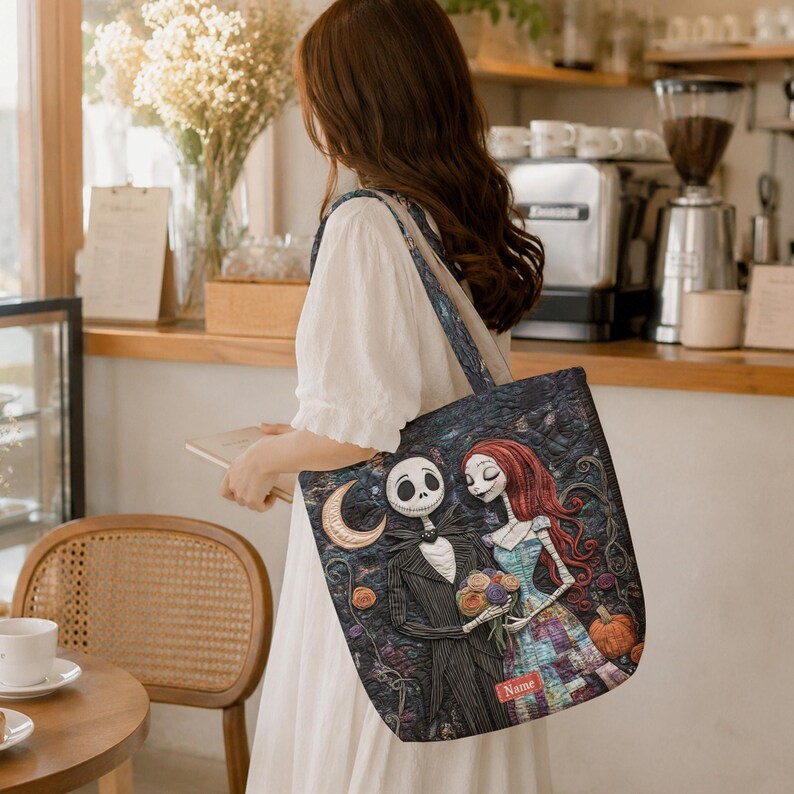 May include: A rectangular tote bag featuring a dark, textured illustration of a skeletal figure in a pinstripe suit and a female figure with long red hair in a patchwork dress. The design includes a crescent moon, pumpkins, and a red name tag.
