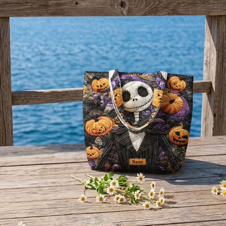 May include: A tote bag featuring a character with a white skull face and a black pinstripe suit, surrounded by orange jack-o'-lantern pumpkins and purple floral patterns. A small rectangular patch with the word Name is centered at the bottom.