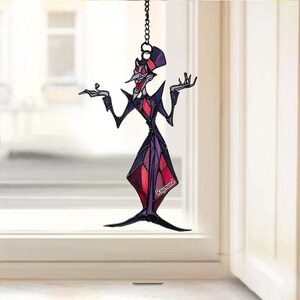 May include: A stained glass suncatcher featuring a cartoon character in a purple, black, and red suit. The character has a long nose and is posed with arms outstretched. The name "Raymond" is printed on the bottom right.