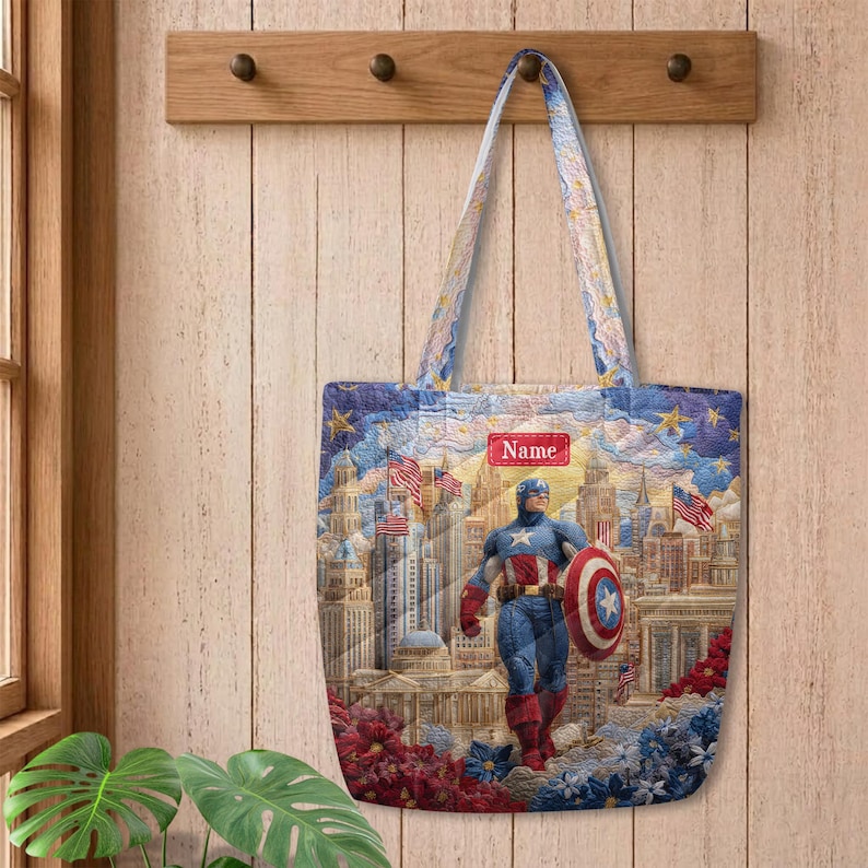 May include: A quilted tote bag featuring a graphic print of Captain America standing in front of a city skyline with American flags. The design includes a red rectangular label with the text Name in white, set against a blue and gold sky.