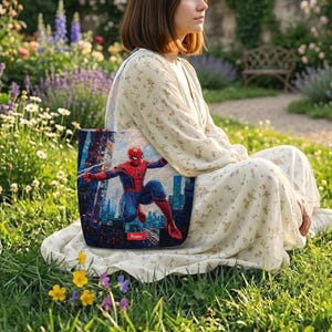 May include: A rectangular fabric tote bag featuring a vibrant graphic print of a superhero in a red and blue suit leaping through a city skyline. The design includes a small red rectangular label at the bottom center with the word Name printed.