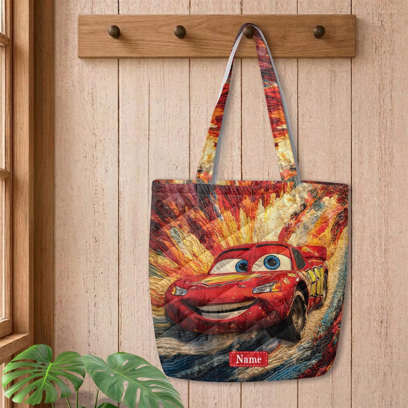 May include: A quilted tote bag featuring a vibrant, multi-colored abstract background with a red race car character. The car has large blue eyes on the windshield and a yellow number on the side. A red rectangular label with the text Name is visible.