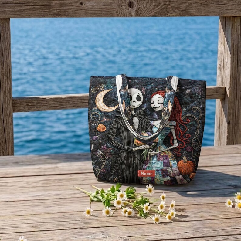 May include: A quilted tote bag featuring a printed illustration of two skeletal figures in a dark landscape with a crescent moon and a pumpkin. The bag has two shoulder straps and a small rectangular red label with the word Name printed on it.