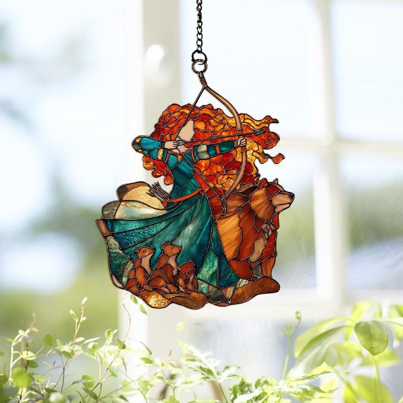 May include: Stained glass suncatcher featuring a woman with red hair aiming a bow and arrow, with a bear and three cubs. The suncatcher has a chain for hanging and is made with shades of teal, orange, and brown.