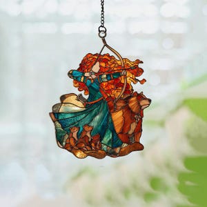 May include: Stained glass suncatcher featuring a woman with fiery red hair aiming a bow and arrow. She is wearing a teal and blue dress, with a bear and three cubs. The suncatcher is suspended by a chain.