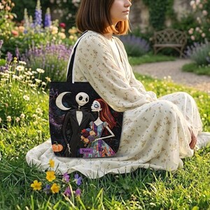 May include: A black tote bag featuring a printed illustration of a skeleton character in a pinstripe suit and a female character with long red hair holding a bouquet of flowers, with a crescent moon, a pumpkin, and a purple name tag label.