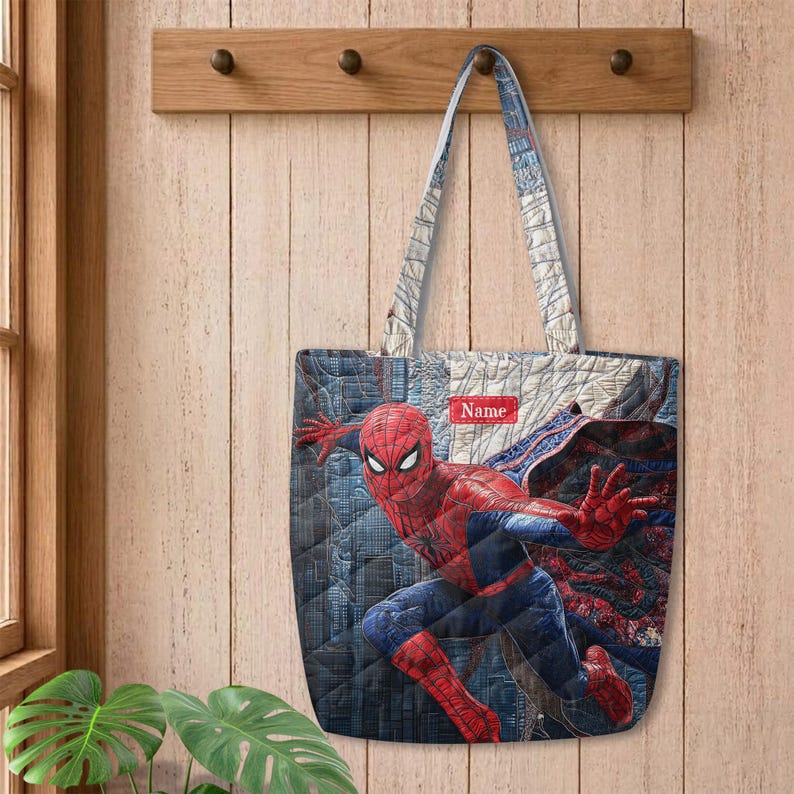 May include: A quilted tote bag featuring a graphic of the superhero Spider-Man in a dynamic pose against a dark blue cityscape background. The bag includes two shoulder straps and a small rectangular red label with the white text Name.